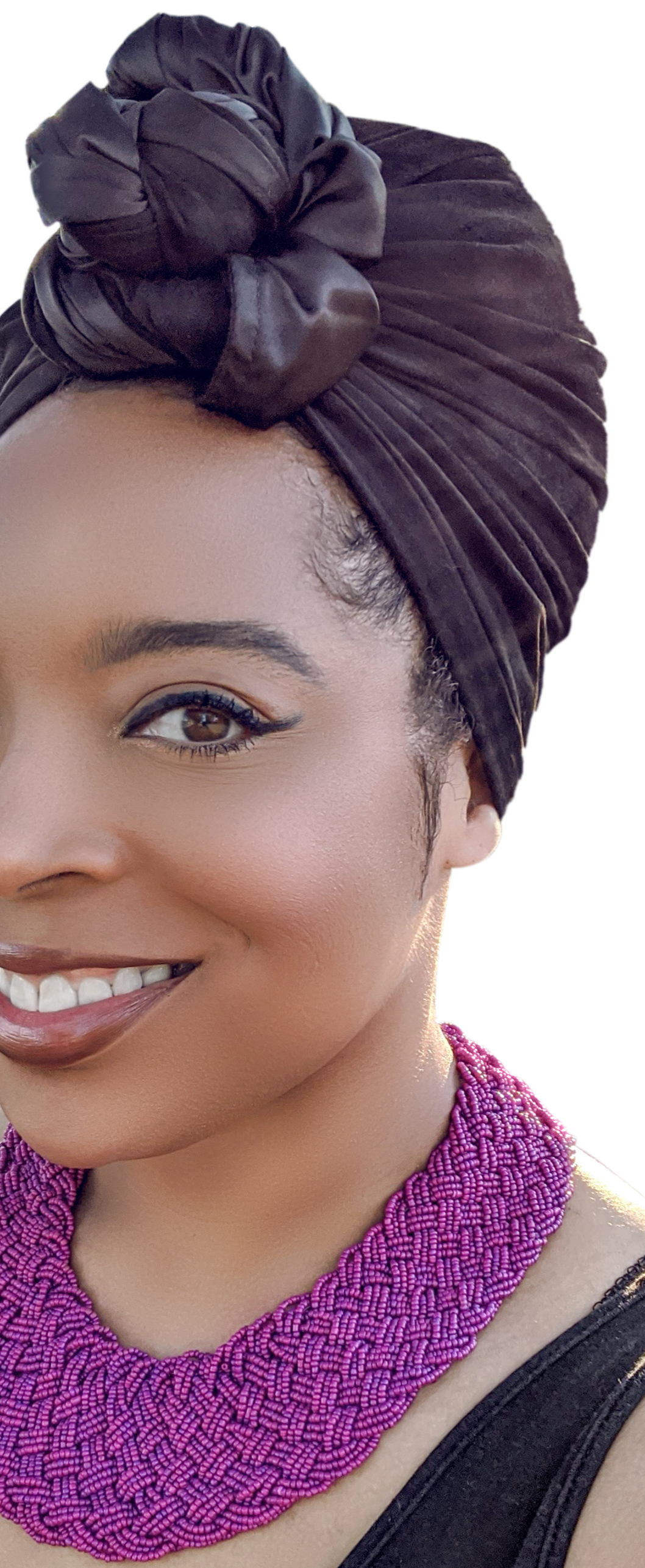 A black woman woman wearing black turban head wrap in a top knot. She is also wearing a beaded purple necklace. Wraptstyle. .