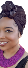 Load image into Gallery viewer, A black woman woman wearing black turban head wrap in a top knot. She is also wearing a beaded purple necklace. Wraptstyle. .
